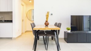 Ein moderner Essbereich mit Holztisch, schwarzen Stühlen, einer Vase mit Trockenblumen, einem kleinen Topfpflanzen und einem Fernseher auf einem Schrank.