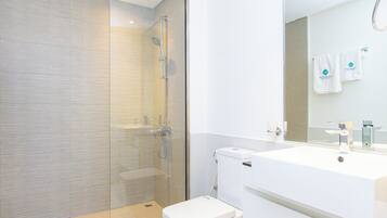 A modern bathroom with a glass shower enclosure, a white sink, and a mirror reflecting a towel.