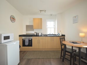Eine kompakte Küche mit Mikrowelle, Backofen und Holzschränken. Ein Fenster sorgt für natürliches Licht und es gibt eine kleine Essecke mit Tisch und Stühlen.