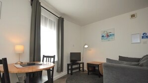 Ein kompakter Wohnraum mit rundem Tisch, einer Couch, einem Fernseher und einem Schreibtisch.