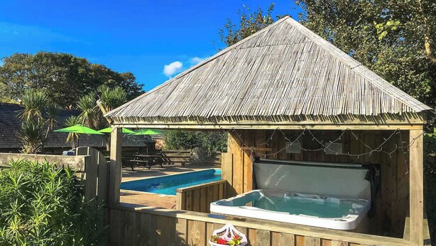 A wooden hot tub with a thatched roof structure, surrounded by a wooden fence and a pool. - Towan Cottage - CWC79064 (Perranporth)