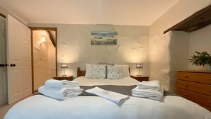 A well-lit bedroom with a large bed, two bedside tables, and a wooden dresser. - Towan Cottage - CWC79064 (Perranporth)