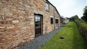 A stone building with a gravel pathway and a grassy area. - Towan Cottage - CWC79064 (Perranporth)