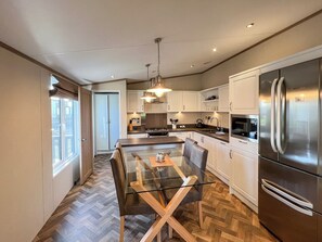 A modern kitchen with a glass dining table, stainless steel appliances, and wooden flooring. - Relax and recharge in this beautiful spacious lodge. (St Andrews)