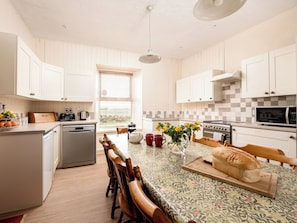 Eine moderne Küche mit weißen Schränken, einer zentralen Kochinsel mit einer blumigen Tischdecke, einem Toaster, einem Wasserkocher und einem Brotlaib auf der Insel.