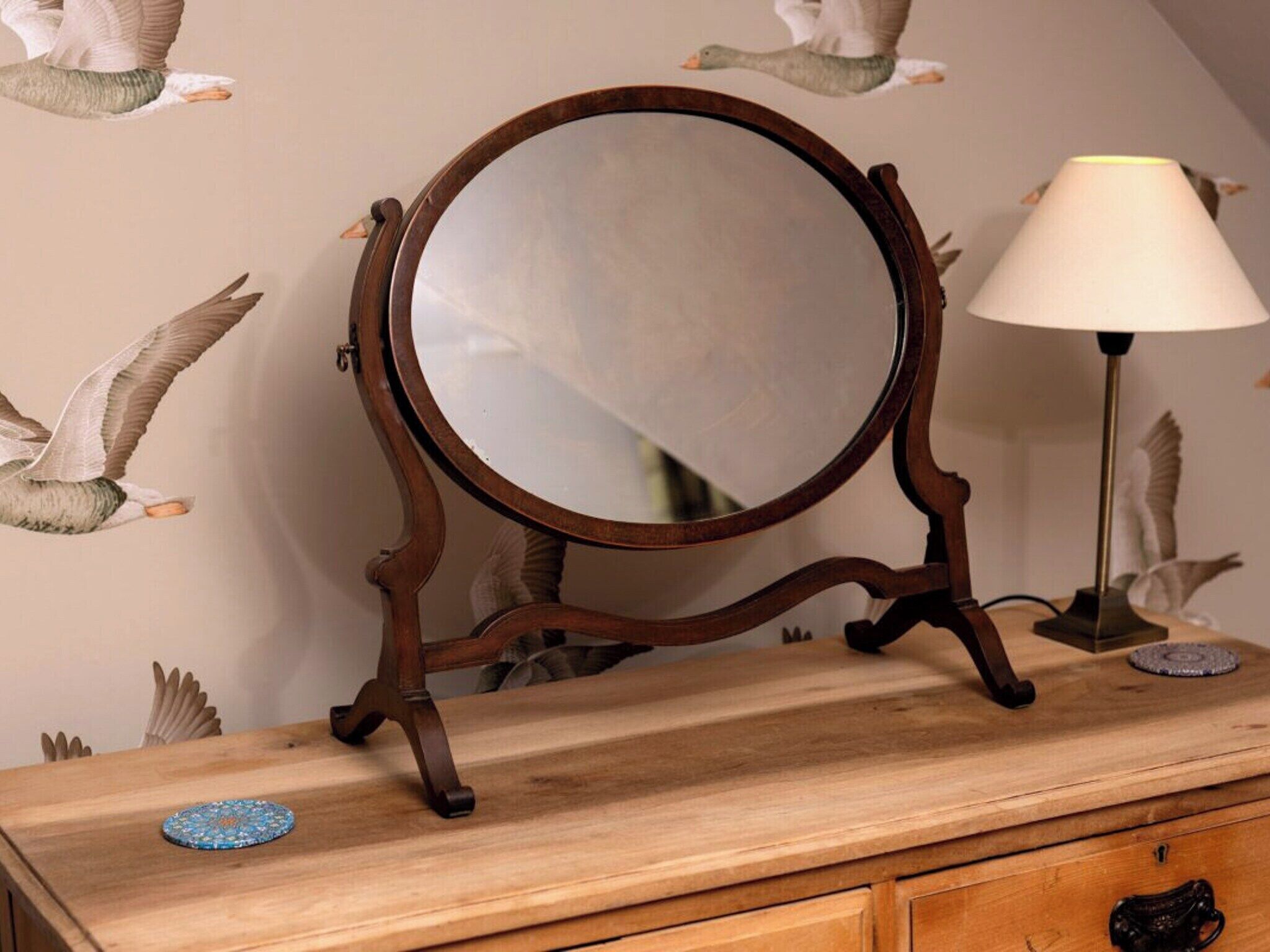 A wooden dresser with a round mirror and a lamp.