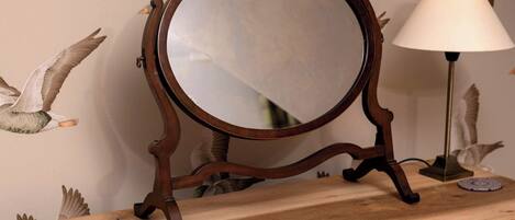 A wooden dresser with a round mirror and a lamp.