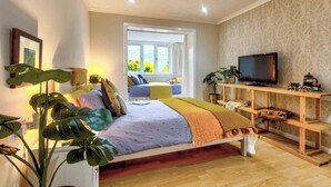 Un dormitorio con cama, plantas en las mesitas de noche, televisor y ventana con vistas.