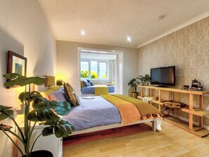 A bedroom with a bed, bedside plants, a TV, and a window with a view.