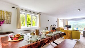 Un comedor con una mesa larga dispuesta para el desayuno, un sofá y un televisor al fondo.
