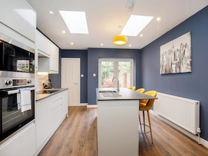 A modern kitchen with white cabinets, a built-in oven, and a central island with yellow chairs. - 2 bedroom accommodation in York (York)