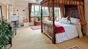 A four-poster canopy bed with a wooden frame and a red throw blanket. There is a fireplace with a white mantel and a bench beside it. A large window with curtains is visible, and a plant is placed near the window. - 2 bedroom accommodation in Troon, near Ayr (Troon, near Ayr)