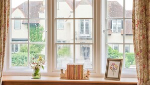 A large window with multiple panes, a small shelf with books and a vase of flowers, and a framed picture. - 2 bedroom accommodation in Troon, near Ayr (Troon, near Ayr)