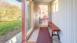 Een gang met een bank, een deur naar een kamer met een bed en uitzicht op een tuin.