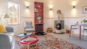 Een gezellige woonkamer met een open haard, een boekenkast, een eethoek en een raam met uitzicht op bomen.