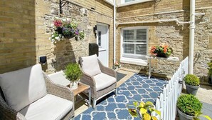 A cozy outdoor seating area with wicker furniture and a patterned rug, surrounded by stone walls and potted plants. - 2 bedroom accommodation in Seaview (Seaview)