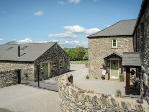 Une charmante maison en pierre avec une allée en gravier, un jardin clôturé et un petit porche agrémenté de plantes en pot.