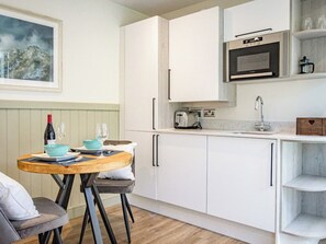A modern kitchen with white cabinets, a built-in oven, and a dining area with a wooden table and chairs. - Whitbarrow - UKC6642 (Windermere)