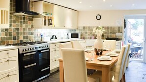 Una cucina moderna con piano cottura a gas, forno, microonde e zoccolo di piastrelle. C'è un tavolo da pranzo con sedie e un vaso di fiori.