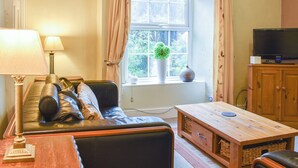 Un salon chaleureux avec un canapé en cuir, une table basse en bois, un téléviseur posé sur un meuble en bois et une fenêtre avec des rideaux.