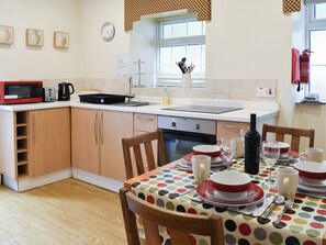 A compact kitchen with a microwave, toaster, kettle, and a small oven. There is a dining table with a polka dot tablecloth and various dishes and glasses. - 2 bedroom accommodation in Beddgelert (Beddgelert)