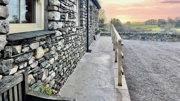 Un edificio in pietra con un portico in legno e un vialetto sterrato che conduce a un muro di pietra.