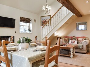 Ein Essbereich mit einem Tisch für vier Personen, einer Treppe, einer Couch und einem an der Wand befestigten Fernseher.