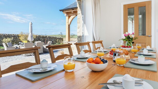 Une table de petit-déjeuner dressée avec des assiettes, des verres et un saladier rempli de fruits, offrant une vue panoramique.