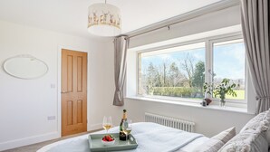Une chambre à coucher avec un lit, une fenêtre avec des rideaux, un lustre et une table de chevet sur laquelle se trouvent une bouteille et des verres.