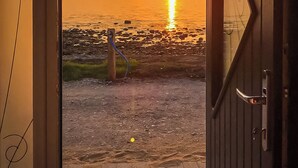 An open door leading to a beach with a sunset view. - Captains Beach House (Aberdesach)