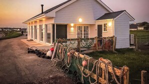 A coastal house with a covered porch, a visible chimney, and a fenced area with fishing equipment. - Captains Beach House (Aberdesach)