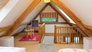 A room with a sloped ceiling, wooden beams, a window with a view, a small table with a chair, and a crib. - 2 bedroom accommodation in Holbeton (Holbeton)