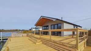 Una casa moderna con terraza de madera, grandes ventanales y vista al agua.