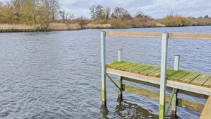 Un muelle de madera se extiende sobre una masa de agua tranquila donde un cisne nada cerca.