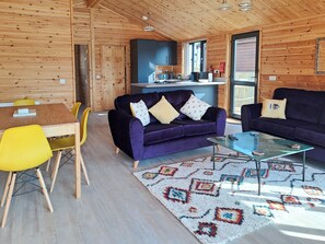 A cozy cabin interior with a dining area, two sofas, a coffee table, and a kitchen area. - 2 bedroom accommodation in Brundall (Brundall)