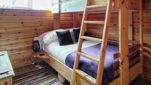 Una cama litera con escalera, un escritorio con silla y una ventana con cortinas.