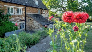 Una casa in pietra con tetto spiovente e un giardino fiorito di fiori rossi.