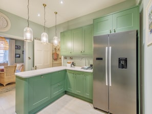 Une cuisine avec des meubles de couleur verte, un réfrigérateur en acier inoxydable et des luminaires suspendus.