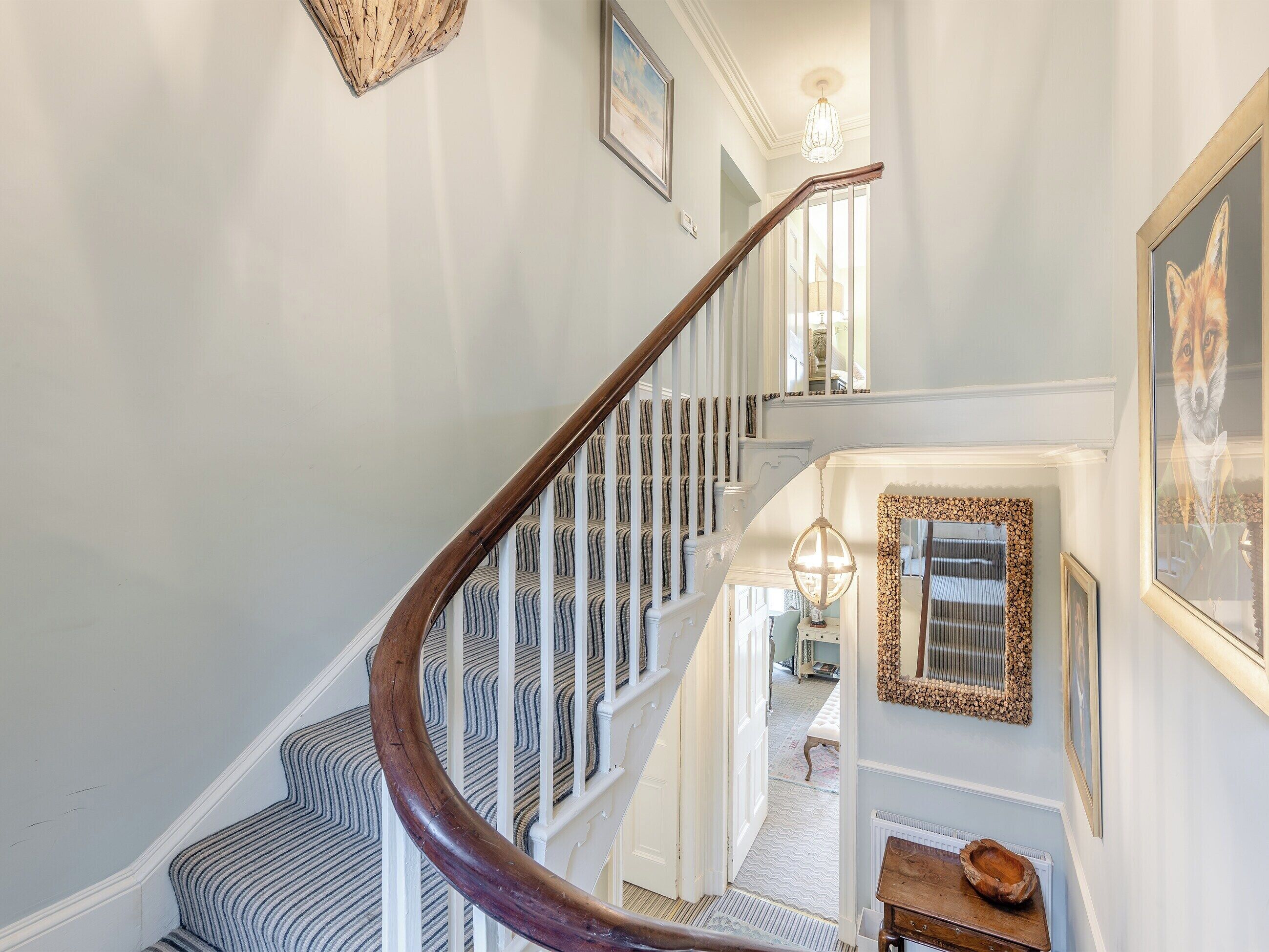 A staircase with a wooden handrail, white balusters, and patterned carpet.