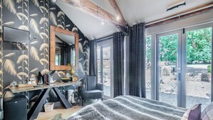 Quarto com uma cama grande, uma escrivaninha com espelho e vista para o jardim pela janela.