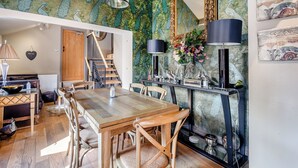 Uma sala de jantar com mesa e cadeiras de madeira, uma escada e um painel decorado com tema de pavão.