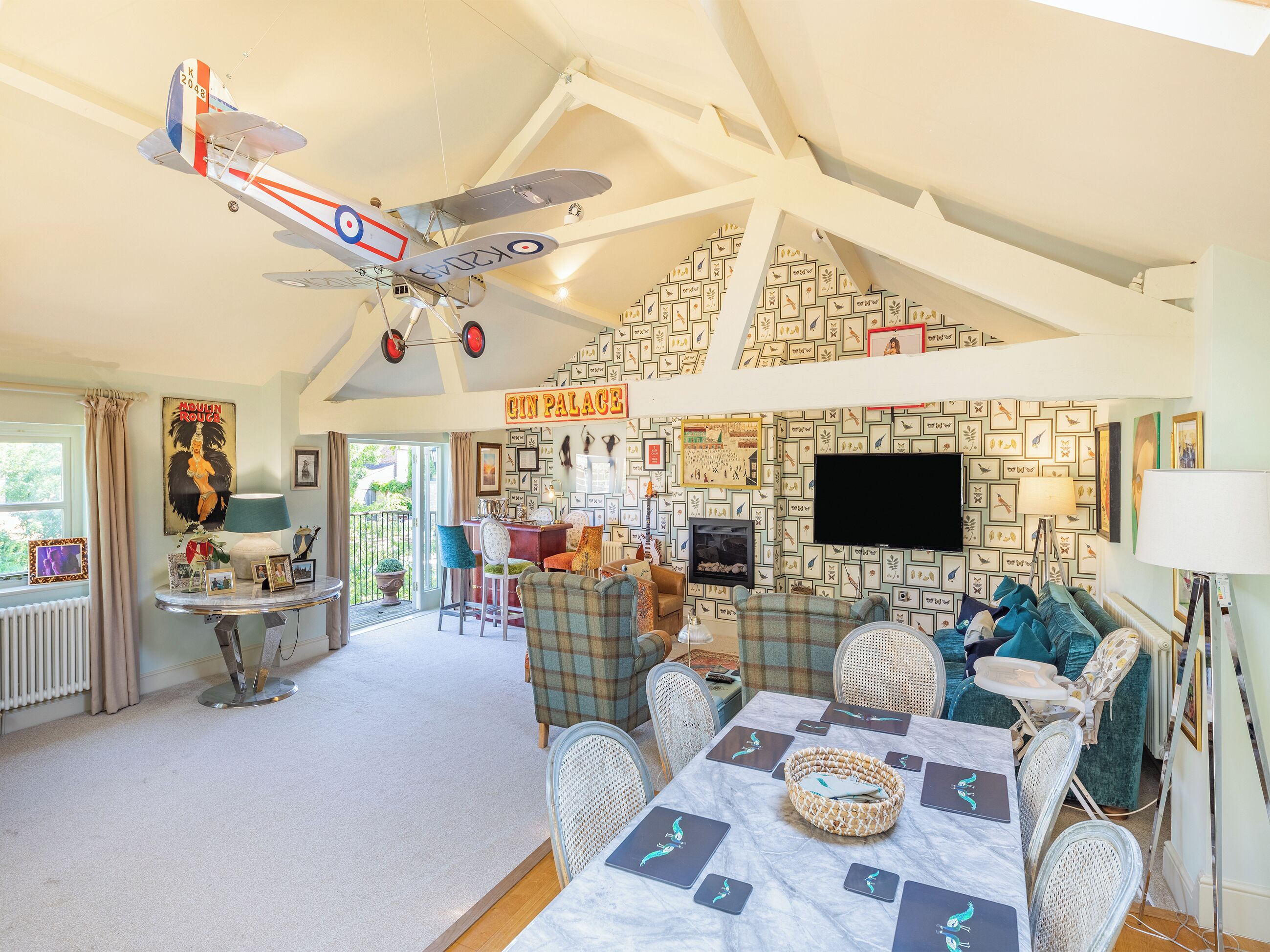 A spacious room with a high ceiling, a dining area with a table set for four, and a large window with curtains.