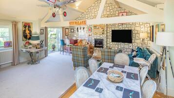 A spacious room with a high ceiling, a dining area with a table set for four, and a large window with curtains.