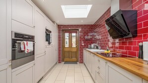 Una cucina moderna con mobili bianchi, zoccolo a parete in piastrelle rosse, forno integrato e piano di lavoro in legno.