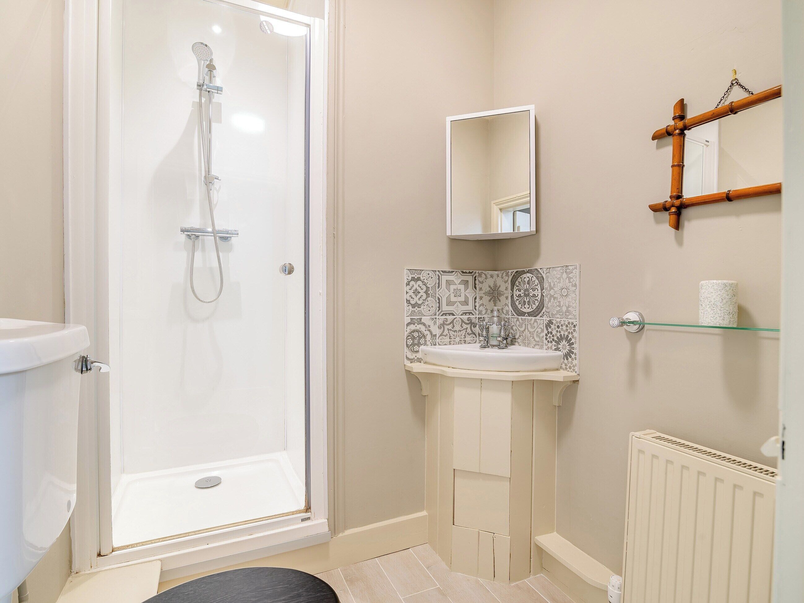 Une salle de bain dotée d’une douche à parois de verre, d’un lavabo blanc, d’un mur recouvert de carreaux derrière le lavabo et d’un miroir au mur.