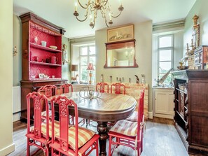 Een eetkamer met een ronde tafel, rode stoelen, een rode boekenkast en een kroonluchter.