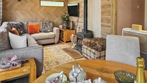 Ein gemütliches Wohnzimmer mit einer Couch, einem Kamin, einem Esstisch gedeckt mit Tellern, einem Teekessel und einer Champagnerflasche.