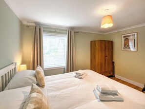 Une chambre d’hôtel avec un grand lit, deux oreillers, une armoire en bois, une fenêtre avec des rideaux et un luminaire fixé au mur.