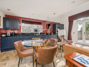A modern kitchen with dark blue cabinets, a red-tiled backsplash, and a dining area with a glass table and leather chairs.