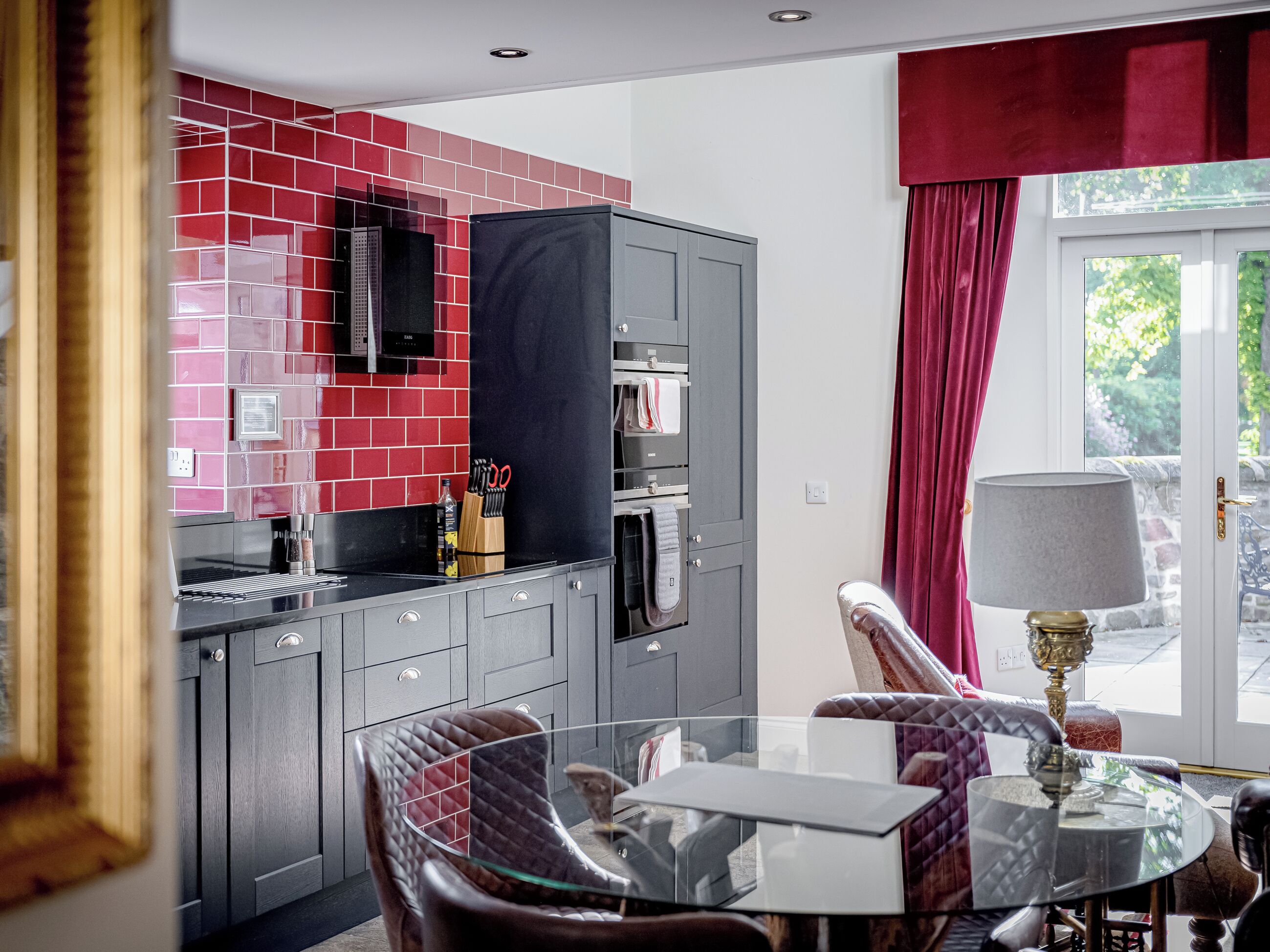 Una cocina moderna con baldosas rojas, microondas empotrado y una mesa de comedor de vidrio con sillas.
